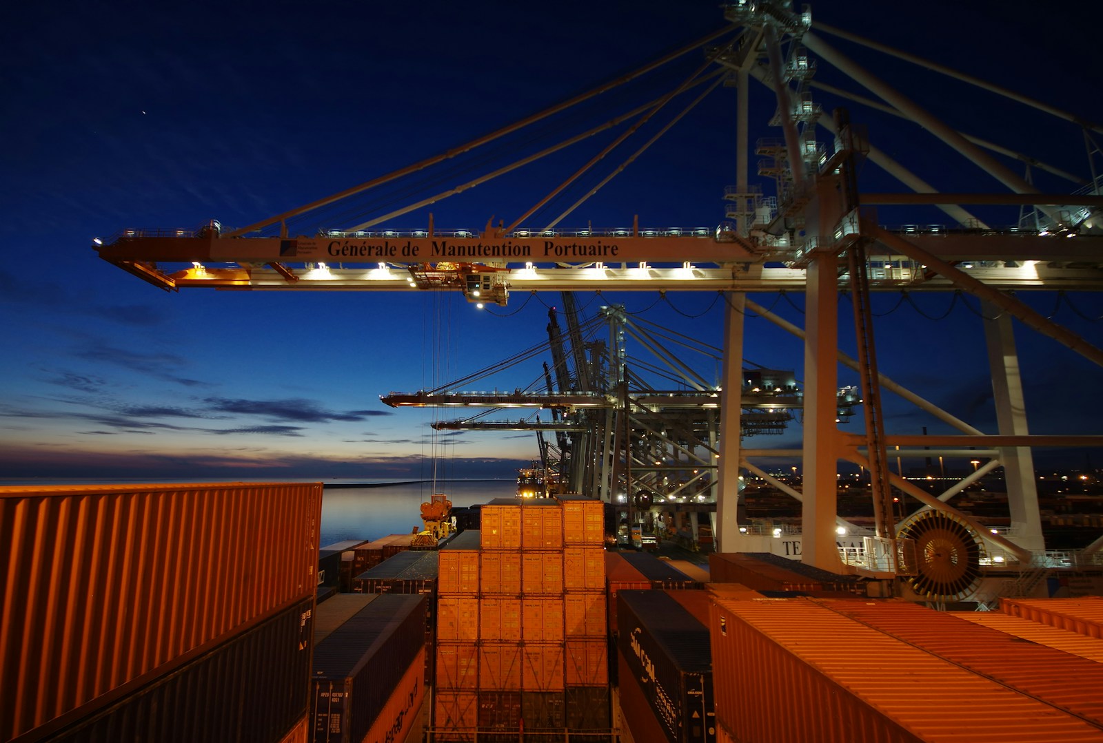 a cargo ship is docked at night with its lights on